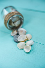 Memories in a small glass jar. Sea shells inside jars and on turquoise wooden background.