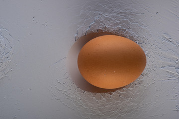 brown egg lies in the print of a hand on the surface of a stone or flour