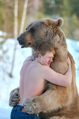 Half-naked caucasian man hugs a brown bear in a winter forest. Bear hugs man in response. Vertical...