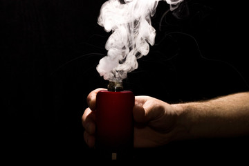 VAPE in a man's hand with a cloud of thick steam on a black background.