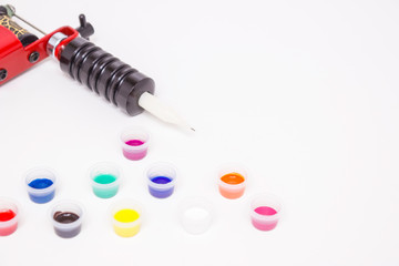Part of the induction tattoo machine and colored paint in disposable plastic jars on a white...