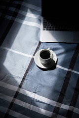 cup of black coffee on a white cup, laptop and light from the window, stay home