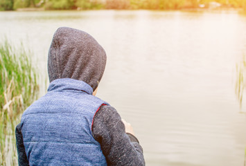 the child in the blue yolk and hood looks into the distance. The boy faces the river and looks at the water. The child walks on the street after the summer rain. The concept of a carefree childhood.