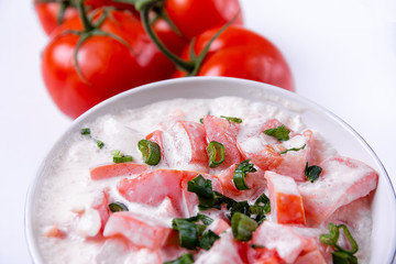 Tomatoes with cream in a bowl and loose tomatoes lying next to it.