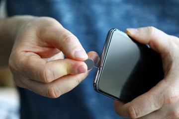 Male hands getting sim card slot of his smartphone out - obrazy, fototapety, plakaty