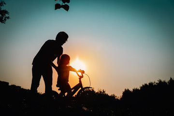 father teaching little daughter to ride bike at sunset nature