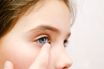 Little girl child putting contact lens into her eye closeup - 343534460