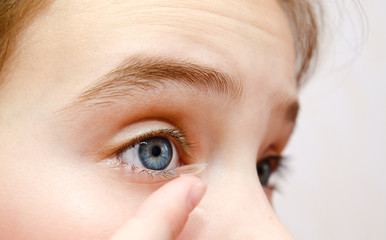 Naklejka premium Little girl child putting contact lens into her eye closeup