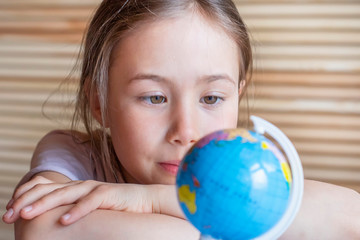 Child girl is smiling and looking at the globe, dreaming about traveling around the world.