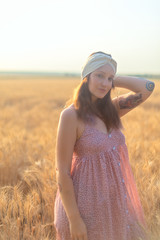 Attractive girl with long brunette hair in long dress and headband on the wheat field at the sunset