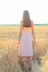 Back view woman with long hair in wheat field at sunset unrecognizable