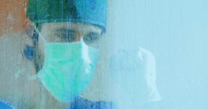 Medico affacciato alla finestra del balcone dell'ospedale durante la pioggia.