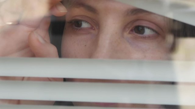 Close-up of a woman's eye looking out into the gap from the blinds. Looking fearfully from the outside, because it is afraid of germs. The concept of quarantine, self-isolation, home isolation.