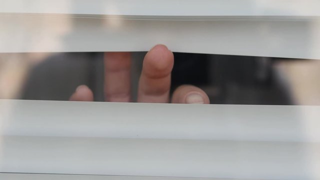 Close-ups of the fingers make a gap from the blinds to let in light into the apartment. Looking from the side is scary because it is afraid of germs. The concept of quarantine, self-isolation, home