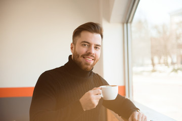Attractive successful young businessman drinking coffee sitting at cafe table.
