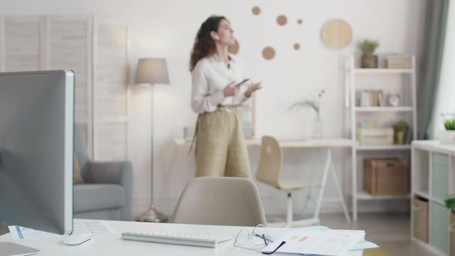Lockdown portrait of young attractive businesswoman wearing elegant clothes and wireless headphones sitting at desktop at computer and discussing documents online
