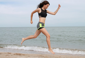 Running young brunette woman. Female running jogging during outdoor workout on the beach. Slim fitness model outdoors