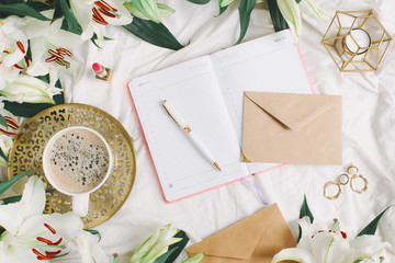 Writing letter on white blanket with coffe cup, notebook, lipstick and many flowers. Flat lay, overhead view