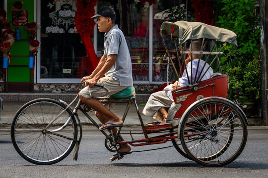 M&auml;nnlicher Rikschafahrer transportiert einen Passagier auf der Stra&szlig;e in Bangkok Thailand