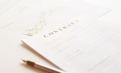 Contract paper and pen on white desk background. Focus on title Contract. Defocused pencil.