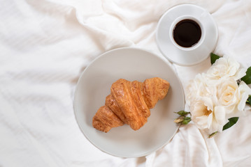 Romantic coffee and croissant with roses in bed. Top view