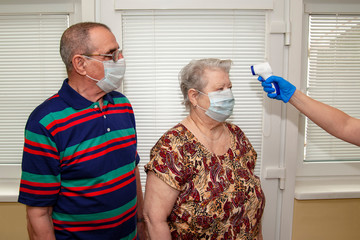 A doctor in blue latex gloves measures body temperature with an infrared emitter for a man and a...