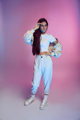 Girl with dark long hair in white sportswear for dancing is smiling on colored background - pink, blue and purple. Concentrated, serious, fashion