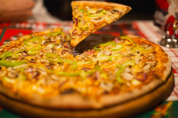 tasty round pizza with a hand taking a piece from it