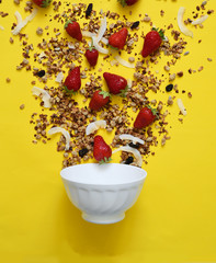 The process of making breakfast. Granola, coconut and strawberries on a yellow background....
