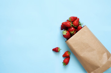 Fresh strawberries in a paper bag on a blue background. Shopping View from above.
