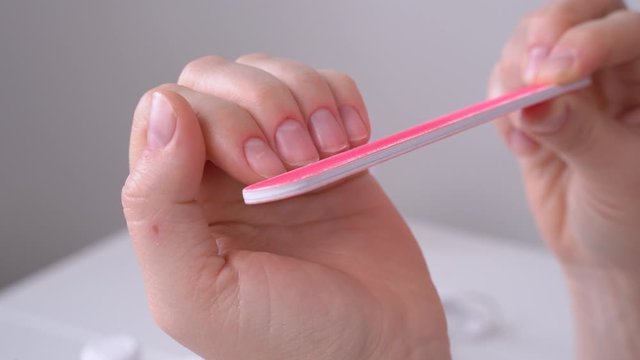 Human changes shape and length of nails on hand with soft pink file, close up. Girl makes herself natural manicure at home during lockdown while all beauty salons are closed.
