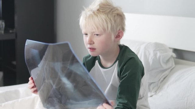 A beautiful blond boy is studying a picture of his lungs in the hospital. The child is discharged from the hospital after the coronavirus.
