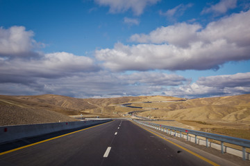 Asphalt road and bright blue sky with fluffy clouds . Empty desert asphalt road from low angle with mountains and clouds on background. road, red desert landscape . Open road with blue clouds .