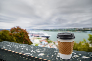 PAPER COFFEE CUP on a wooden railing, Port of Quebec City in blur. Cruise liner and city on the background. Close up and selective focus