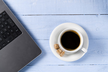 Laptop with cup of coffee on light blue old wooden table. Notebook with cup of fresh coffee in home office. Working from home concept