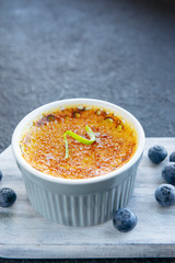 Creme brulee - traditional french vanilla cream dessert with caramelised sugar on top, blueberries and lime pile on rustic white wooden board, dark table. Sweet dessert -custard. Copy space.