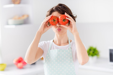 Photo of housewife attractive lady arms holding two big tomato hiding eyes sending air kisses playful mood enjoy morning cooking tasty dinner wear apron stand modern kitchen indoors