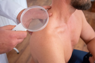 Patient bei einer Hautkrebsvorsorgeuntersuchung mit Lupe