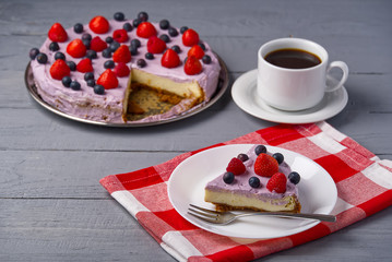 Piece of home made Cheesecake with berries on plate and mug of Americano coffee. Cheesecake with Strawberry, blueberry and raspberry on grey wooden background.