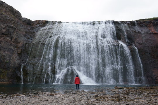 junge Frau in roter Jacke vor einem Wasserfall in Island