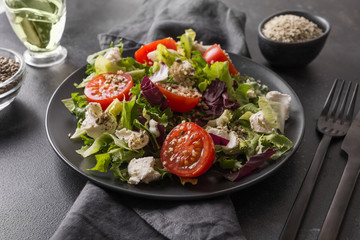Healthy vegan salad in black dish with fresh tomato, greens, seeds hemp for clean eating. Close up.