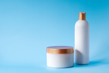 White jar and a bottle with golden caps on a blue background. Body and hair care, beauty copy space