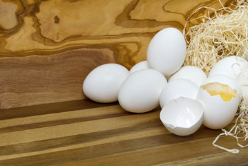 White chicken eggs and broken eggs on wooden board or table.