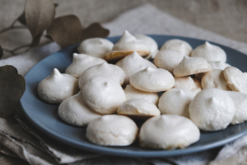 Homemade meringue cookies. White baked meringues with texture and cracks in the foreground on blue plate. Closeup 