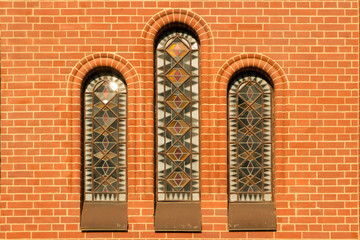 three narrow windows with colored stained-glass windows in a red brick catalytic church