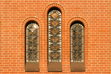 Fototapeta premium three narrow windows with colored stained-glass windows in a red brick catalytic church