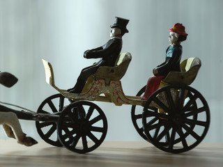 Fototapeta premium Vintage figurine - horses harnessed to a cart with a coachman and a passenger. Cart close-up.