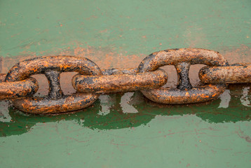 Fengdu, China - May 8, 2010: Closeup of 5-piece heavy brown-red rusty metal chain link on wet green...