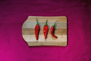 three red hot peppers on board in still life, top view, with magenta background