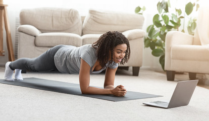 Fit black woman training at home, watching online tutorial on laptop